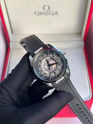 Omeg* svart klocka med gummiband - Snygg Omega-klocka med svart gummiband och silverfärgat boett. Urtavlan har detaljer i svart, silver och vitt samt världsstäder runt om. Baksidan har genomskinligt fönster som visar urverket. Perfekt för dig som gillar exklusiva accessoarer.