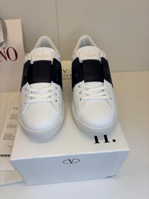 Valentino Opens strl 42 - Eleganta och helt nya sneakers från Valentino Garavani i tidlös vit design med sofistikerade svarta detaljer. En ikonisk modell som kombinerar lyx och minimalism.  ✔️ Storlek 42✔️ Helt nya, med box & tillbehör  En exklusiv sneaker för dig som uppskattar kvalitet och stil.  📩 Vid seriöst intresse