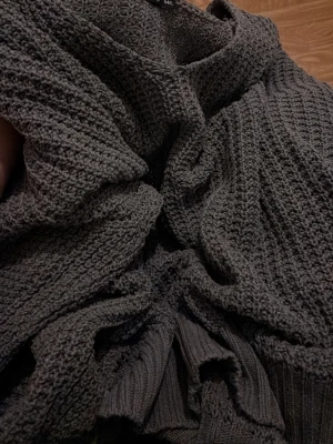 Grå stickad tröja med v-ringning - Mysig grå stickad tröja med v-ringad hals och grovstickad struktur. Tröjan är väldigt over-size. Har några små trådar som sticker ut. Den är en mer neutral grå färg i verkligheten.