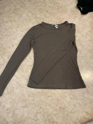 Brun långärmad topp från H&M - En enkel och stilren brun långärmad topp från H&M. Modellen är figurnära med rund halsringning och tillverkad i mjukt bomullsmaterial. Perfekt att matcha med jeans eller kjol för en clean look.