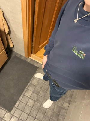 Mörkblå sweatshirt La Chemise Lacoste - Mörkblå sweatshirt från Lacoste med klassisk rund halsringning och ribbade muddar vid ärmslut och midja. Fin Lacoste-logga med krokodil broderad på bröstet i grönt och gult. Perfekt för en clean och stilren look.