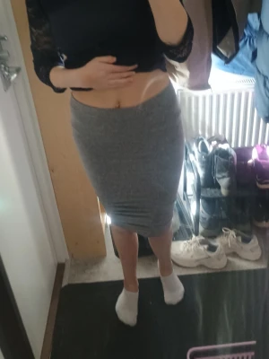 Grå tight kjol i bomull - Säljer en enkel och stilren grå tight kjol i mjukt bomullsmaterial. Kjolen är midilång och har en kroppsnära passform som framhäver figuren. Perfekt att matcha med crop tops eller stickade tröjor för en trendig look.