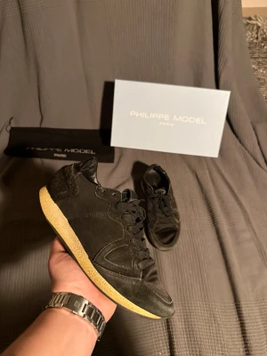 Svarta Philippe  - Snygga svarta sneakers från Philippe Model med klassisk låg siluett. Skorna har ovandel i mocka och textil, svarta skosnören och en kontrasterande beige sula. Perfekta för dig som gillar stilrena och exklusiva sneakers med en unik touch.