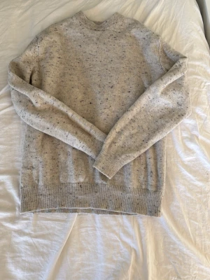 Beige stickad tröja från Vailent - Mysig beige stickad tröja från Vailent i storlek S. Tröjan har en klassisk rund halsringning och är dekorerad med små färgstänk för en cool, avslappnad look. Perfekt att matcha med jeans eller kjol för en enkel men snygg outfit.