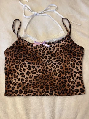Leopardmönstrad croppad topp med spets - Snygg croppad topp med leopardmönster, tunna axelband och vit spetsdetalj upptill. Toppen har en liten rosett framtill och knytband i nacken.