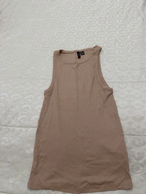 Beige ribbad linnetopp från Vero Moda - Säljer en beige ribbad linnetopp från Vero Moda. Toppen är ärmlös med rund halsringning och har en slim passform. Perfekt att styla med jeans eller kjol för en enkel och clean look.