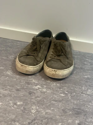 Mörkgröna Philippe modell skor med mocka - Säljer ett par mörkbruna philppe modell skor i mocka med klassisk låg profil och vita gummisulor. Skorna har matchande bruna skosnören och en enkel, stilren design som passar till det mesta. Perfekta för dig som gillar en clean och avslappnad look.