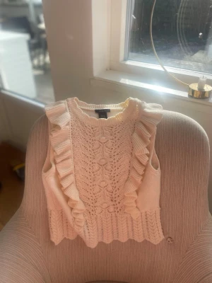 Vit stickad topp med volanger - Supersöt vit stickad topp med volangdetaljer längs axlarna och ett fint spetsmönster framtill. Storleken är XS och är i väldigt fint skick, superfin till sommaren 