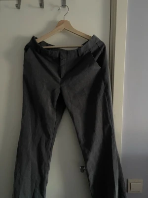 Gråa utsvängda kostym byxor  - Snygga mörkgrå kostymbyxor med klassisk rak passform och pressveck. Byxorna har hällor för skärp och diskreta sidofickor. Perfekta för en stilren look. Materialet ser ut att vara en blandning av polyester och viskos.