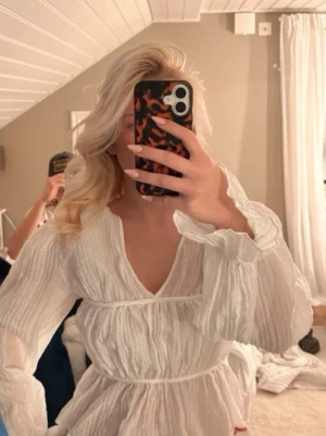 Vit blus med volang - Säljer en superfin vit blus med volangdetaljer och v-ringning. Blusen har långa, luftiga ärmar och markerad midja som ger en snygg siluett. Perfekt för sommarens alla tillfällen!