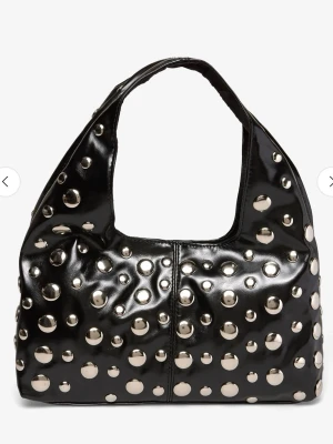 Svart handväska med silvriga nitar - Cool svart handväska i glansigt material med stora silvriga nitar över hela väskan. Väskan har en mjuk, lite puffig form och bred axelrem. 