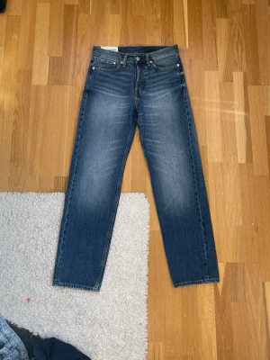 Blå raka jeans med vintage tvätt - Säljer ett par blå jeans med rak passform och snygg vintage tvätt. Jeansen har klassiska fem fickor, normal midja och subtila slitningar framtill för en avslappnad look. Perfekta till sneakers eller boots och passar till det mesta i garderoben.