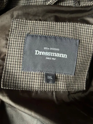 Brunrutigt pufferjacka Dressmann 3XL - Säljer en brunrutigt pufferjacka från Dressmann i storlek 3XL. Jackan har huva, dragkedja framtill och två sidofickor. Materialet är quiltat och mönstret är diskret rutigt i bruna och beige toner. Perfekt för kalla vinterdagar.