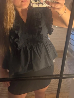 Svart volangblus  - Snygg svart blus med volangdetaljer längs bröstet och axlarna. Blusen har knappar framtill och en lätt utsvängd passform nedtill. Köpt för 559kr. Pris kan diskuteras💗