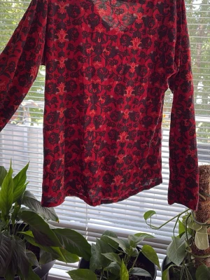 Röd blus med svart mönster och twist - Snygg röd blus med svart och mörkrött blommigt mönster. Blusen har långa ärmar och en twistdetalj vid ringningen framtill. Tunt, lätt material som känns luftigt och skönt. Perfekt för dig som gillar färg och mönster!