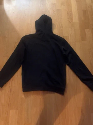 Svart hoodie med vita snören - Passar perfekt för S. En stilren svart hoodie med huva och vita dragsnören. Hoodien har lång ärm och en klassisk känguruficka framtill. Perfekt för en avslappnad look och enkel att matcha med andra plagg.
