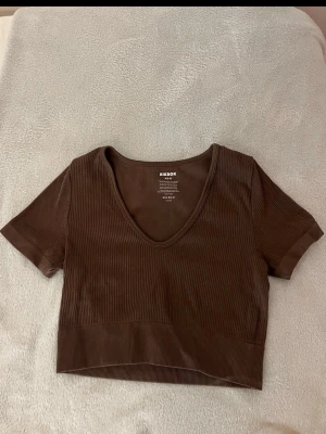 Brun ribbad croppad topp BikBok - Snygg brun croppad topp från BikBok med ribbad struktur och djup v-ringning. Kortärmad och i stretchigt material som sitter bekvämt. 
