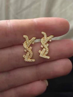 Guldiga örhängen - Säljer ett par helt nya stilrena örhängen i guldton med gnistrande stenar och logga. Örhängena har en elegant design och är rostfria. Perfekta för dig som gillar lyxig och trendig stil💛