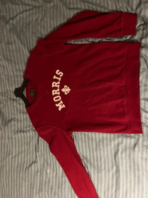 Röd sweatshirt från Morris - Röd sweatshirt från Morris med vit text och logga på bröstet. Klassisk rund halsringning och långa ärmar. Perfekt för en avslappnad och stilren look. Tillverkad i mjukt material för extra komfort.