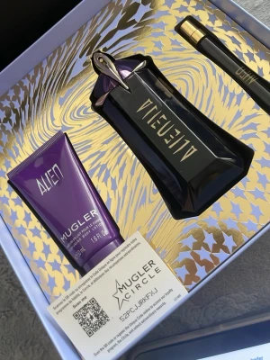 Alien parfymset från Mugler - Exklusivt parfymset från Mugler med Alien-doft. Innehåller en mörklila parfymflaska med gulddetaljer, en matchande body lotion i tub samt en smal sprayflaska. Allt levereras i en snygg presentförpackning med guldmönster och stjärnor.