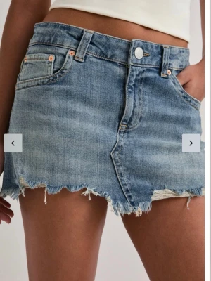 Blå jeanskjol från Nelly - Snygg blå jeanskjol från Nelly med rå, fransig kant och klassisk femficksdesign. Kjolen har en kort passform och stängs med knapp och dragkedja framtill. Perfekt för en trendig och avslappnad look. Nästan helt ny bara använd några gånger! Stl 34