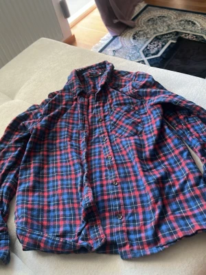 Rutig blå och röd skjorta - Klassisk långärmad skjorta i blått och rött rutigt mönster. Skjortan har knappar framtill och en bröstficka. Perfekt för en avslappnad och cool stil.
