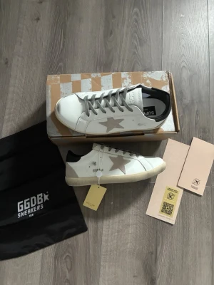 Vita GGDB sneakers med stjärna - Snygga vita sneakers från GGDB med grå stjärna på sidan och grå skosnören. Skorna har svart detalj på hälen och beige sula🤩 Hör av er vid snabbaffär samt funderingar