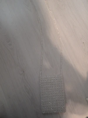 Transparent pärlkuvertväska - Säljer en unik kuvertväska helt täckt av transparenta pärlor. Väskan har en rektangulär form och ett långt axelband i samma pärlmaterial. Perfekt accessoar för att lyfta din outfit med en glittrig touch.
