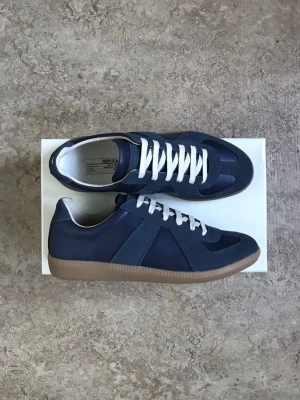 Maison Margiela gats - Ett par väldigt snygga mm gats i färgen pewter/ navy. Skorna är tillverkade med äkta läder vilket gör skorna snyggare med tiden, även att de formas till din fot, perfekt till sommaren om man vill ha något stilren och lowkey. Dessa par är i nyskick. Priset är ej hugget i sten!