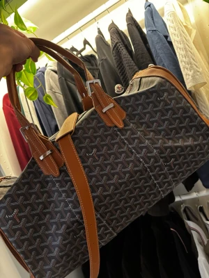 Mönstrad weekendbag med bruna detaljer - Snygg weekendbag med klassiskt svart och grått mönster och bruna läderdetaljer. Väskan har dubbla handtag, silverfärgade spännen och dragkedja. Insidan är fodrad i gult tyg och väskan har en rymlig form, perfekt för resor.