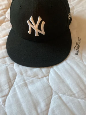 Svart New Era Yankees keps 59FIFTY - Snygg svart keps från New Era med klassiskt New York Yankees broderat vitt NY-logga framtill. Modellen är 59FIFTY med rak skärm och broderade ventilationshål. Perfekt för dig som gillar streetwear och sportig stil.