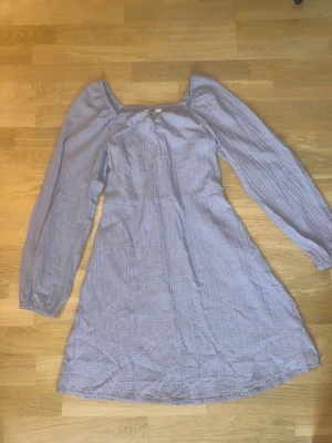 Ljuslila långärmad klänning - Söt ljuslila klänning med lång ärm och lätt rynkad struktur. Klänningen har en markerad midja och en något utställd kjol. Fyrkantig ringning och mjukt, tunt tyg som ger en luftig känsla. EUR 164. Perfekt för dig som gillar en romantisk och enkel stil.