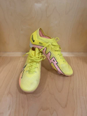 Gula Nike Air Zoom fotbollsskor - Säljer ett par riktigt snygga fotbollsskor från Nike i en skarp gul färg med rosa och svarta detaljer. Skorna har textilovandel, snörning och AIR ZOOM-tryck på sidan.  Dom är använda 1-2 gånger och är i storlek 42.