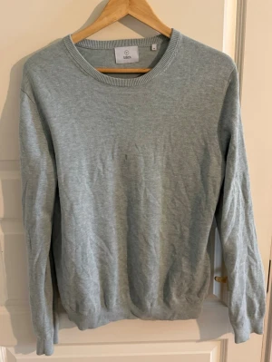 Turkos stickad tröja från Bläck - Snygg ljusgrå stickad tröja från Bläck med rund halsringning och ribbade muddar vid ärmslut och nederkant. Enkel och stilren design som passar perfekt till jeans eller chinos. Materialet känns mjukt och bekvämt mot huden.