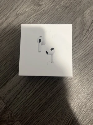 Apple AirPods med laddningsetui - Säljer ett par vita Apple AirPods med trådlöst laddningsetui. Hörlurarna har en stilren och kompakt design i plast och passar perfekt för dig som vill ha smidiga och trådlösa hörlurar till mobilen. Levereras i originalförpackning.