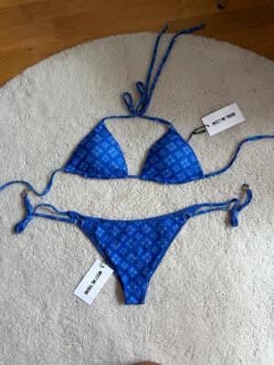 Blå bikini med snörning - Snygg blå bikini med vita småmönster och knyt i både topp och trosa. Klassisk trekantsmodell med tunna band som ger en trendig look. Perfekt för lata dagar på stranden eller poolen.