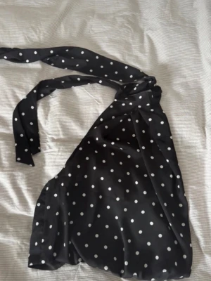 Svart prickig halterneck topp - Snygg svart halterneck topp från h&m med vita prickar och knyt i nacken. Toppen är ärmlös och har en croppad passform som ger en trendig look. 🖤