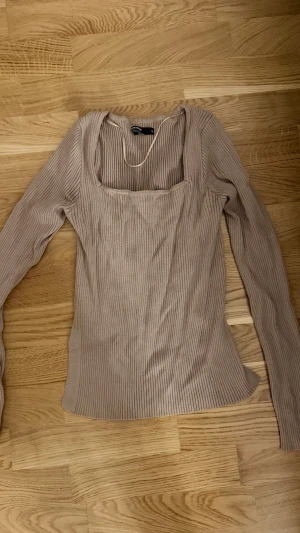 Beige ribbad långärmad topp - Snygg beige ribbad topp med lång ärm och fyrkantig ringning. Toppen har en slim passform och är perfekt att styla med jeans eller kjol. Materialet är mjukt och stretchigt för en bekväm känsla.