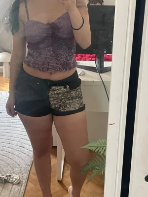 Lågmidjade jeansshorts plus topp❤️ - Säljer ett par svarta shorts med en stor silvrig paljettdetalj på ena sidan framtill. Shortsen har låg midja och knappstängning. Toppen är mesh