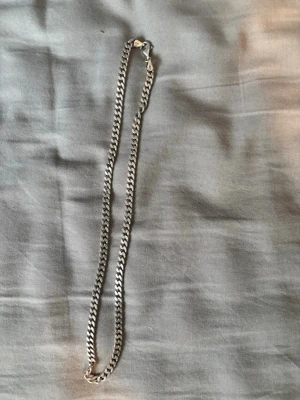 Kedjehalsband i äkta silver - Säljer ett stilrent halsband i äkta silver (stämplat 925) med klassisk pansarkedja och karbinlås. Halsbandet har en tidlös design och passar perfekt till olika stilar. Längden är medellång och länkarna är platta och breda.
