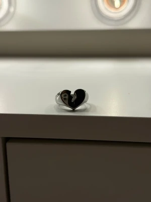 Silvrig ring med brustet hjärta - Unik ring i silverfärgad metall med ett hjärta som har en bruten design i mitten. Hjärtat är centrerat och ringen har en modern, edgy känsla. Perfekt för dig som gillar statement-smycken och vill sticka ut lite extra.