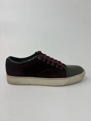 Vinröda Lanvin och grå sneakers med lackad tå - Sneakers med vinröd mocka, grå lackad tå och matchande vinröda skosnören. Yttersulan är vit och skon har en klassisk låg profil. Perfekt för dig som vill sticka ut med en unik färgkombo och snygga detaljer.
