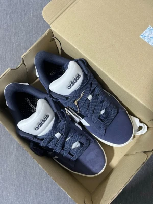 Mörkblå Adidas sneakers Cloudfoam - Snygga mörkblå sneakers från Adidas med Cloudfoam-sula för extra komfort. Skorna har vita detaljer, breda mörkblå snören och en vit sula. Märkeslogga på plösen och sidan. Perfekta för en sportig och avslappnad stil. Med extra snöre vit hel ny inte använd nån gång nu med pris lapp 