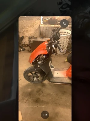 Röd scooter utan kåpa fram - En röd scooter med svart sadel och grå fotplatta. Främre kåpan saknas och delar av styret är synliga. Scootern har sportig design och är tillverkad i plast och metall. Perfekt för dig som gillar att meka eller behöver reservdelar.