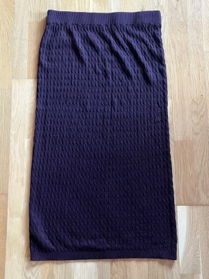 Mörklila/ mörkröd stickad långkjol - Säljer en mörklila/ mörkröd långkjol med stickad struktur och bred resår i midjan. Kjolen har ett diskret mönster och är perfekt för dig som gillar en enkel men ändå unik stil. Passar till både sneakers och boots.