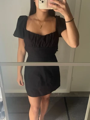 Svart kort klänning med öppen rygg - Supersnygg svart kort klänning med puffärmar, fyrkantig urringning och öppen rygg med snörningsdetaljer. Perfekt för dig som vill sticka ut med en trendig och stilren look.