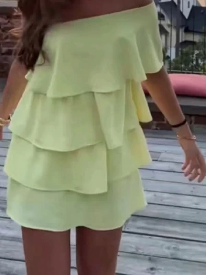 Gul offshoulder volangklänning - Säljer en ljusgul kortklänning med offshoulder och flera lager volanger. Perfekt för sommarens alla tillfällen och ger en riktigt fräsch vibe. Klänningen är ärmlös och har en lös passform som känns både luftig och trendig. Lånad bild men inga alls defekter på