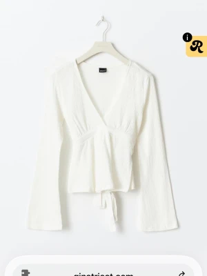 Vit omlottopp från Gina Tricot - Snygg vit omlottopp från Gina Tricot med lång ärm och v-ringning. Toppen har knyt i midjan och är tillverkad i ett lätt, strukturerat material som ger en fräsch och modern look. Perfekt att styla med jeans eller kjol. SLUTASÅLD på hemsidan 💗