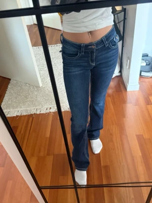 Mörkblå bootcut jeans med låg midja - Säljer ett par mörkblå bootcut jeans med låg midja och kontrastsömmar. Jeansen har klassiska fem fickor och snygg tvätt med lätt slitning. Perfekta för dig som gillar en trendig och avslappnad stil. De är från gina tricot ! Köpt från barn sidan så storleken är 164 vilket motsvarar xs ungefär och jag är 167 cm lång om någon undrar !
