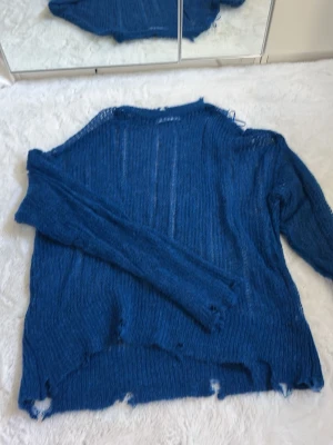Blå stickad tröja från Zara - Säljer en blå stickad tröja från Zara med oversize-passform och transparent, grovstickad struktur. Tröjan har långa ärmar och råa kanter för en avslappnad look. Perfekt för lager-på-lager-stil.